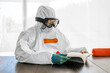 © Westend61 - Woman, wearing protective clothes, sitting at table, reading book