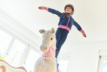 Girl Standing On Play Horse At Home
