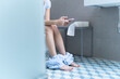 © Eloisa Ramos/Westend61 - Young woman sitting on toilet and using smartphone