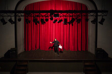 Rehearsing Actor With Script Standing On Theatre Stage In Front Of Red Curtain