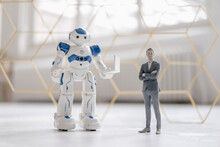 Miniature Businessman Figurine Standing Next To Robot With Laptop