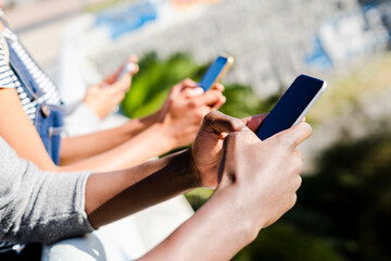 Friends standing side by side, using smartphones