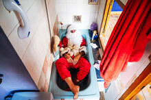 Man Wearing Santa Claus Costume Lying In Bathtub At Home