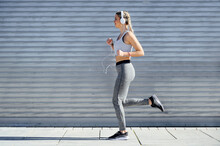 Female Athlete Wearing Headphones Jogging Against Shutter