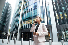 Businesswoman Talking On Mobile Phone While Standing Against Modern Office Skyscraper In Financial District