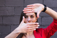 Businesswoman With Gray Eyes Making Finger Frame Against Purple Brick Wall