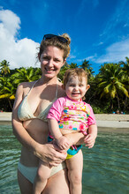 Portrait Of Smiling Mother Holding Cute Daughter While Standing In Sea Against Sky, British Virgin Islands