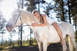 © SERGIO NIEVAS/Westend61 - Full length portrait of young woman leaning on white horse in forest