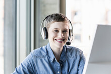 Portrait Of Smiling Businesswoman Wearing Headset At Desk In Office