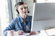 © UWE_UMSTAETTER/Westend61 - Businesswoman wearing headset at desk in office taking notes