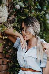 Poster - Vertical shot of a young Caucasian lady wearing a shirt-dress with accessories leaning on a wall