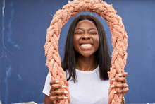 Portrait Of Grinning Young Woman Holding Rope In Front Of Blue Background