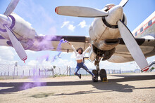 Carefree Young Woman Enjoying While Holding Distress Flare With Purple Smoke Against Airplane At Airport Runway