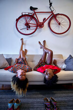 Two Women Lying Relaxed On The Sofa In The Living Room With Vintage Bicycle Hanging On The Wall