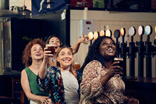 Excited Female Friends Sitting At The Counter In A Pub Watching Tv