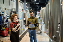Man And Woman Working In Craft Brewery Discussing Quality Of A Beer