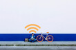 © Xavier Lorenzo/Westend61 - Man in casuals using laptop on sidewalk while sitting at Wi-fi symbol by bicycle against white wall