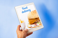 Food Delivery Concept, Food Ordering On Internet Via Tablet. Man Holding Tablet On Blue Background