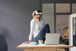 © Robijn Page/Westend61 - Young businesswoman sitting on desk in office wearing VR glasses