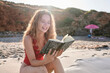 © IVAN GENER/Westend61 - Happy young woman reading book on the beach