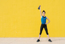 Young Woman Exercising With Dumbbell In Front Of A Yellow Wall