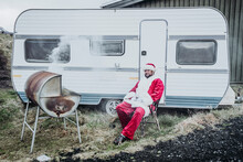 Iceland, Santa Claus Sitting In Front Of Caravan Barbecueing