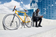 © Juan Novakosky/Westend61 - Man with yellow bicycle sitting on stairs, using smartphone, Barcelona, Spain