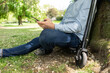 © Joseffson/Westend61 - Man sitting on E-Scooter in a park leaning against tree trunk while using smartphone, partial view