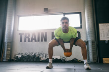 Male Athlete Looking Away While Lifting Kettlebell In Health Club