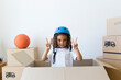 © SusPons/Westend61 - Portrait of girl wearing bicycle helmet looking out of cardboard box at new home