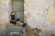 © Petra Stockhausen/Westend61 - Italy, Tuscany, Monteriggioni, woman sitting at house entrance using laptop