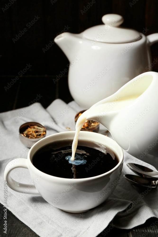 Pouring of milk in cup with black tea on table