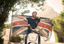 Man With Arms Outstretched Holding National Flag While Sitting On Motorcycle During Summer