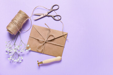 Envelope with rope, scissors, flowers and stamp on lilac background