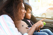 Little girl with toy fastened in car safety seat and her mother pointing at something on road