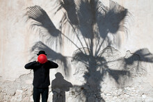 Morocco, Essaouira, Man Wearing A Bowler Hat Holding Red Balloon In Front Of His Face At A Wall