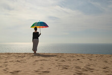 Woman With Colorful Umbrella Standing At The Beach, Rear View