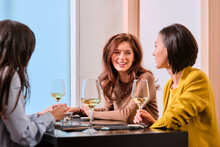 Young Female Friends With Wine Glasses While Sitting At Table In Restaurant
