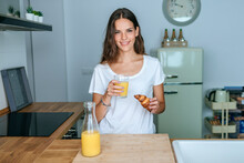Portrait Of Smiling Young Woman Having Breakfast With Juice And Croissant In The Kitchen