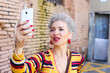 © Retales Botijero/Westend61 - Portrait of mature woman with red lips and grey hair taking selfie with cell phone