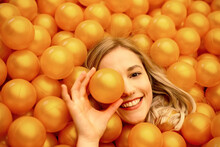Close-up Of Smiling Beautiful Woman Lying In Orange Ball Pit