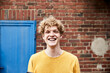 © Westend61 - Portrait of young man with curly blond hair in front of brick wall