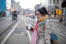 Beautiful Woman With Disposable Cup Crossing Road At Street During Winter