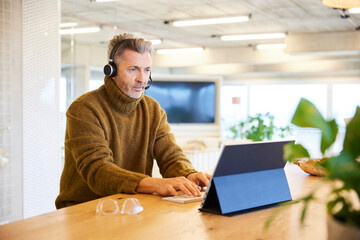 Businessman wearing headset talking while working on digital tablet at office