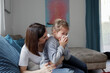 © Katharina Mikhrin/Westend61 - Mother sitting with daughter blowing her nose on couch in living room at home
