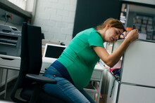 Exhausted Pregnant Woman Sitting At Desk In Office