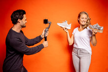 Man Holding Gimbal With Mobile Phone While Photographing Woman Showing Shoes Against Orange Background