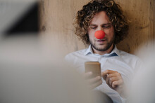 Businessman With Red Clown Nose Using Cell Phone In Office