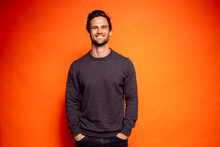 Happy handsome man with hands in pockets against orange background