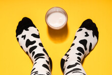 Man's Foot With Cow Print Socks And Glass Of Milk On Yellow Background In Studio
